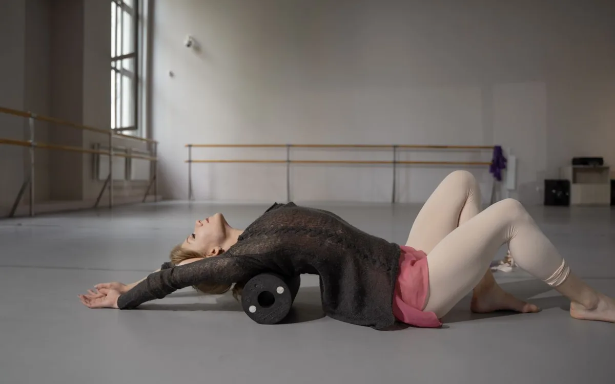 A woman uses a foam roller while stretching her back on a floor.