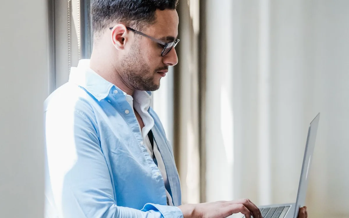 Man standing at a window while working on a laptop