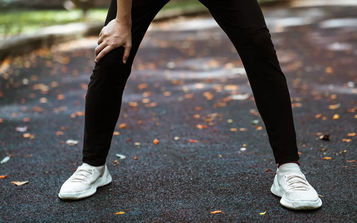 Runner resting with hands on knees beside a leaf-covered path