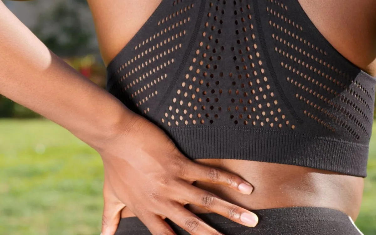 A woman places a hand on her lower back outdoors.