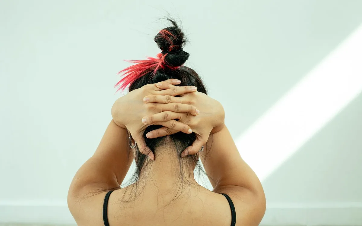 A woman clasps her hands behind her head during a neck stretch.