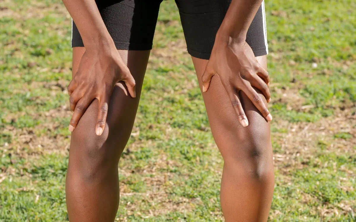 A person outdoors rests their hands on their knees.