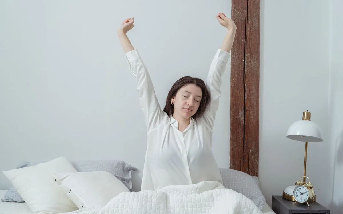 Woman stretching her arms while sitting in bed