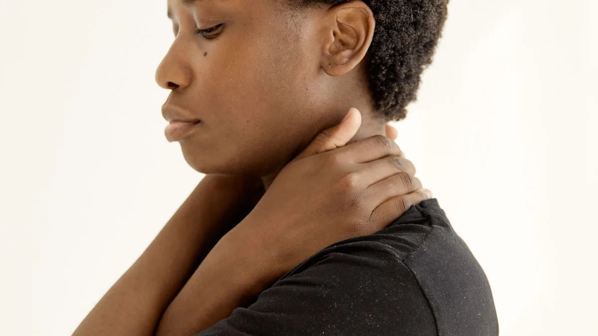 A woman in a black shirt touching her neck.