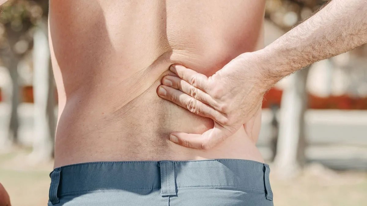 A man holding his lower back outdoors.