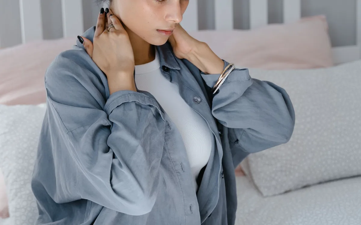 Woman sitting on a bed with a hand on her neck