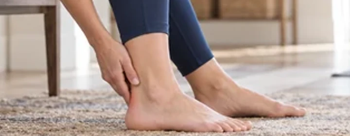 Woman reaching toward her sore ankle